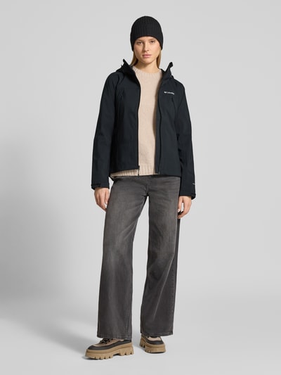 Frauenmodel trägt Regenjacke mit Omni-Tech™ ECO-Technologie von Columbia in Schwarz, mit Kapuze, Reißverschlüssen und Reißverschlusstaschen, Ganzkörperansicht von vorne.
