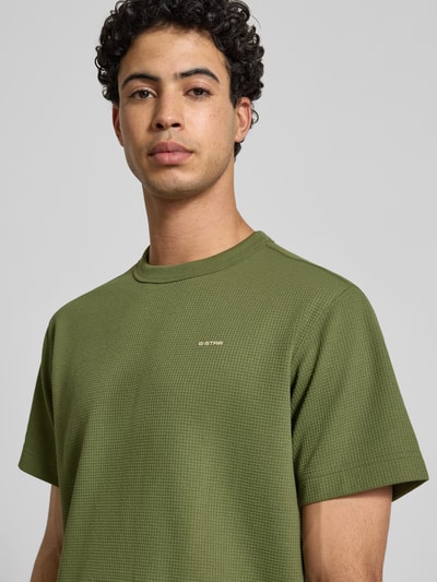 Männermodel trägt Regular Fit T-Shirt mit Strukturmuster von G-Star Raw in Olivgrün, Rundhalsausschnitt, Logo, Nahaufnahme Oberkörper. Herren T-Shirt, Rückenlänge bei Größe M: 71 cm.