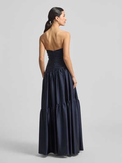 Modelka nosi Regular Fit Abendkleid in Falten-Optik od Luxuar, granatowy satynowy materiał, krój regular fit, fason w talii, dekolt odkryte ramiona, A-linia, długość tyłu w rozmiarze 36: 125 cm, szerokość w rozmiarze 36: 41 cm, tekstura plisowana, zamek na szwie, widok całej sylwetki z tyłu.