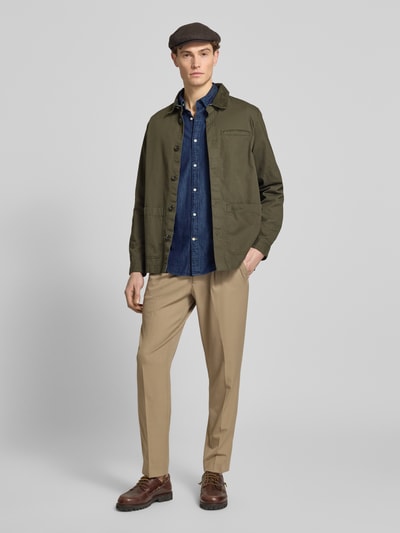 Männermodel trägt Slim Fit Jeanshemd aus reiner Baumwolle von Barbour, tkanina stylizowana na denim, krój slim fit, kołnierzyk typu button down, listwa guzikowa na całej długości, wyhaftowane logo, długi rękaw, mankiet zapinany na 1 guzik, lekko zaokrąglone wykończenie, bawełna, Ganzkörperansicht von vorne.