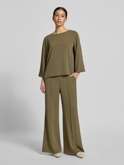 Vrouwenmodel draagt stoffen broek met elastische band van comma, flared fit, elastische materiaalmix, siernaden, kleur olijfgroen. Ganzkörperansicht von vorne.