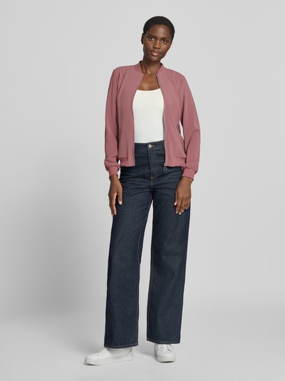 Kobiece model nosi Regular Fit Blouson mit Allover-Muster model 'COCO' od VERO MODA, jasnoróżowy, proste formy, matowa tekstura, bomberka damska, Ganzkörperansicht von vorne.