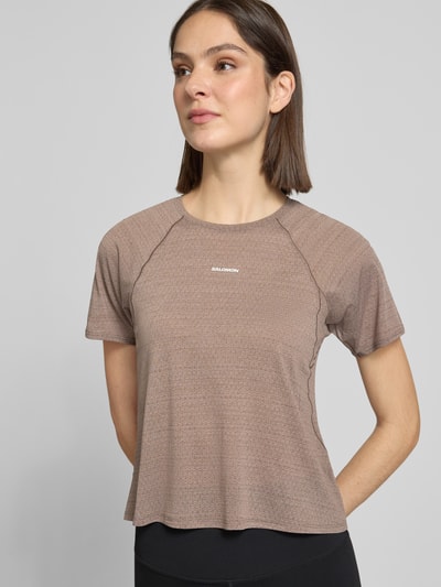 Frauenmodel trägt Cropped Fit T-Shirt mit Logo-Print von Salomon, braun, Rundhalsausschnitt, kurzärmelig, Nahaufnahme Oberkörper.