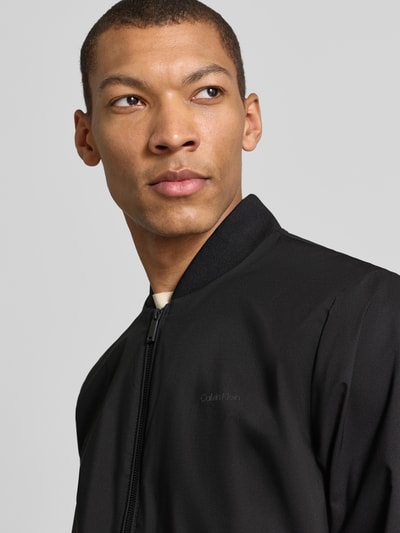 Männermodel trägt schwarze Bomberjacke mit Reißverschlusstaschen Modell 'MATTE' von CK Calvin Klein, Nahaufnahme Oberkörper. Gerader Schnitt, kurzer Stehkragen, elastische Abschlüsse, Rückenlänge 67 cm, Schulterbreite 47 cm, Brustweite 58 cm, Ärmellänge 68 cm.