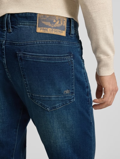 Männermodel trägt Jeans mit Label-Detail Modell 'Tailwheel JEA' von PME Legend, Baumwollmischung mit Stretch-Anteil, 5-Pocket-Design, Slim-Fit, mittleres Blau, sichtbare Label-Details und Used-Optik, Nahaufnahme Rückansicht.