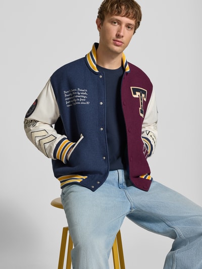 Männermodel trägt Regular Fit Bomberjacke aus Woll-Mix Modell 'LETTERMAN' von Tommy Jeans in Blau, Weiß und Bordeaux, Herren Bomberjacke / Blouson, Nahaufnahme Oberkörper.