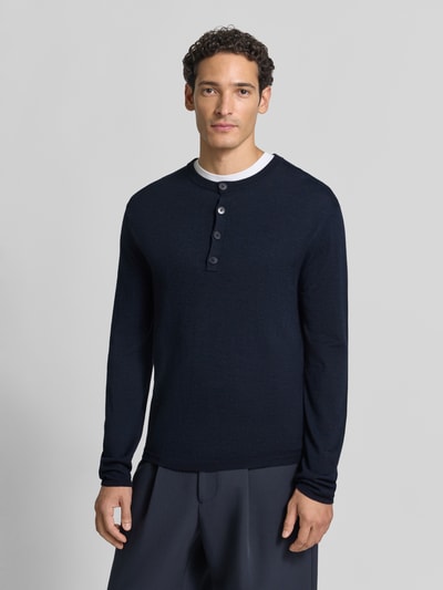 Männermodel trägt Strickpullover mit Henley-Kragen von DRYKORN aus reiner Baumwolle, dunkelblau, gerippte Abschlüsse, Ganzkörperansicht von vorne.