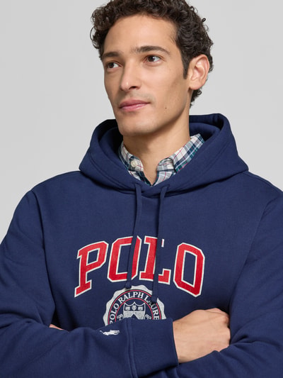 Männermodel trägt Relaxed Fit Hoodie aus Baumwoll-Mix von Polo Ralph Lauren in Dunkelblau, weiße und rote Details, Nahaufnahme Oberkörper. Herren Sweatshirt von Polo Ralph Lauren