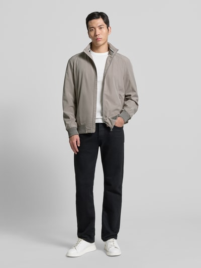 Męski model nosi Jacke mit Stehkragen von Christian Berg Men, szary kolor, prosty fason, materiał z dodatkiem stretchu, stojący kołnierz, zamek błyskawiczny, kieszenie na zamek, prążkowane wykończenia, długość tyłu 28 cm, szerokość ramion 18 cm, szerokość klatki 20 cm, długość rękawa 26 cm, widok całej sylwetki z przodu.