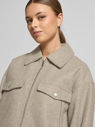 Modelka kobieca ma na sobie Regular Fit Hemdjacke mit Reißverschluss Modell 'FORTUNEFREJ' od Vero Moda, filcowa struktura, jednolity kolor, kołnierzyk koszulowy, zapięcie na zamek, długie rękawy, kieszenie z patkami, krój regular fit, zbliżenie na górną część ciała.