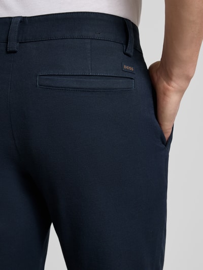Männermodel trägt Tapered Fit Chino aus Baumwoll-Mix Modell 'CHINO PLEATED' von BOSS Orange, unifarben, Twill-Textur, Nahaufnahme Rückansicht.