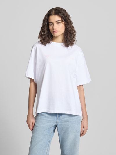 Frauenmodel trägt Oversized T-Shirt mit Motiv- und Logo-Print Modell 'NIVELLES' von Pegador aus reiner Baumwolle, weiße Farbe, lockere Passform, dezenter Print, Rundhalsausschnitt, überschnittene Schultern, Ganzkörperansicht von vorne.
