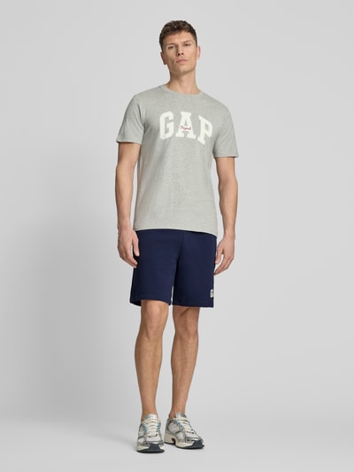 Männermodel trägt Sweatshorts mit elastischem Bund von GAP, Baumwoll-Mix, Relaxed-Fit, Logo, dunkelblau, Ganzkörperansicht von vorne.