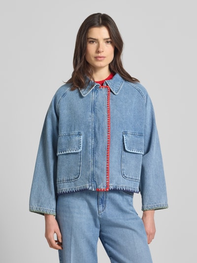 Kobiece model prezentuje kurtka jeansowa z haftem i kieszeniami z patką 'Jeansjacke mit Stitching und Pattentaschen' od Amber & June, wykonana z czystej bawełny, pudełkowy krój, wykładany kołnierz, długość tyłu w rozmiarze 36: 56 cm, szerokość ramion: 46 cm, szerokość klatki piersiowej: 63 cm, długość rękawów: 55 cm, jasnoniebieski denim, widoczne czerwone detale haftu, miękka faktura, widok całej sylwetki z przodu