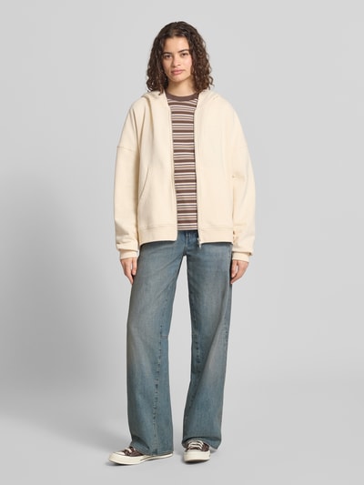 Modelka kobieca ma na sobie Oversized Sweatjacke mit Zweiwege-Reißverschluss Model 'Flower' od OH APRIL z bawełny, z kapturem, wyhaftowanym logo i kieszenią kangurka, krój oversized, widok całej sylwetki z przodu