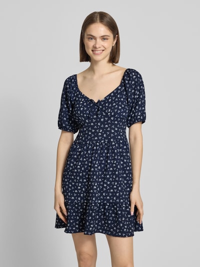 Frauenmodel trägt Minikleid mit Puffärmeln Modell 'HILLARY' von Only, florales Allover-Muster, Schleife, Crêpe, Tailliert, Mini-Länge, Karree-Ausschnitt, Ganzkörperansicht von vorne.