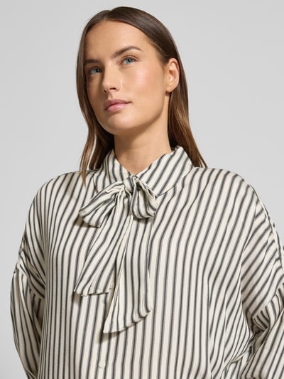 Frauenmodel trägt Hemdbluse mit Knopfleiste Modell 'Ruby' von Mustang aus reinem Modal, Streifenmuster, Schleifen-Detail, lockerer Schnitt, Nahaufnahme Oberkörper.