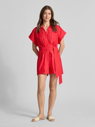 Frauenmodel trägt Jumpsuit in Wickel-Optik Modell 'TRACY' von SUNCOO PARIS in Rot, Reine Baumwolle, Relaxed-Fit, Lochstickerei, Bindegürtel, Ganzkörperansicht von vorne.
