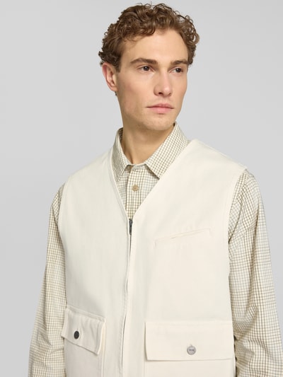 Männermodel trägt Weste mit Zweiwege-Reißverschluss Modell 'Bow' von Wood Wood aus reiner Baumwolle, krój relaxed fit, V-Ausschnitt, Pattentaschen, crema und beige Töne, Struktur aus glattem Stoff, Szerokość w rozmiarze M: 56 cm, długość tyłu: 66 cm, szerokość ramion: 45 cm, Nahaufnahme Oberkörper.