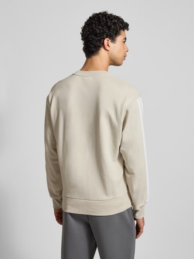 Männermodel trägt Sweatshirt mit Label-Stitching von adidas Sportswear in Beige, Baumwoll-Mix mit Viskose-Anteil, lockerer Schnitt, Gerippte-Abschlüsse, Rundhalsausschnitt, Rückenlänge 68 cm, Ärmellänge 62 cm, Ganzkörperansicht Rückansicht.