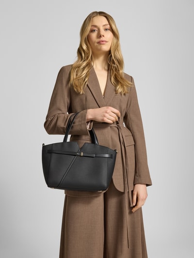 Frauenmodel trägt Henkeltasche aus Rindsleder Modell 'REVERS' von BOSS in Schwarz, rechteckige Form, dezente Textur, Ganzkörperansicht von vorne.