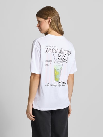 Männermodel trägt damski t-shirt z bawełny JJXX model 'LATTE', krój loose fit, okrągły dekolt, długość tyłu w rozmiarze S: 65 cm, biel z nadrukiem, tekstura gładka, całkowity widok od tyłu.