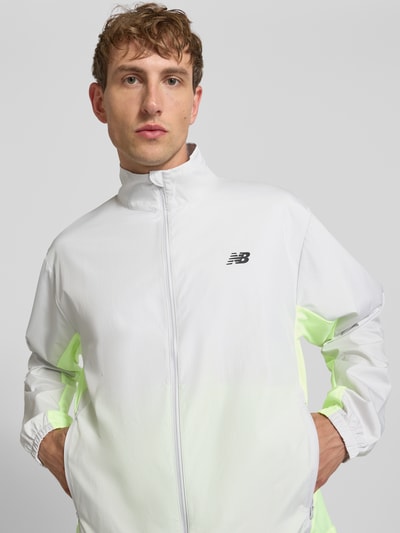 Männermodel trägt Regular Fit Jacke in Stehkragen Modell 'Fast Days' von New Balance in Weiß mit Logo-Print, Reißverschluss, Eingrifftaschen, elastischen Ärmelabschlüssen und Tunnelzug im Bund, Rückenlänge 68 cm, Ärmellänge 66 cm, Nahaufnahme Oberkörper.