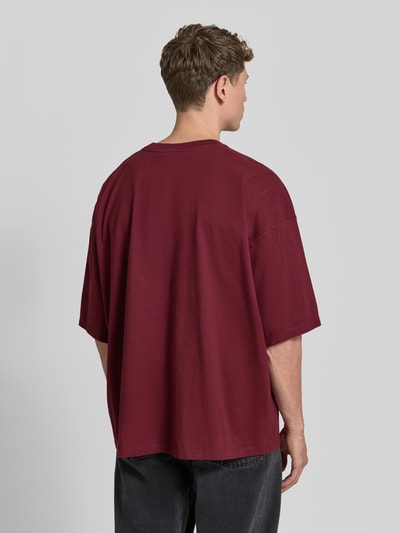 Männermodel trägt T-Shirt mit Logo-Print Modell 'GIXY' von American Vintage, bordeauxrot, Loose Fit, reine Baumwolle, Ganzkörperansicht Rückansicht.