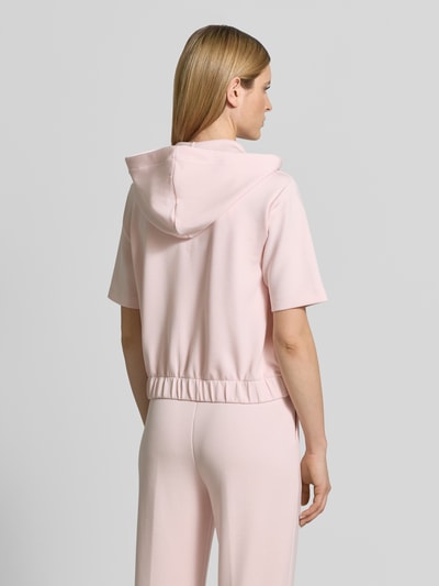 Frauenmodel trägt Sweatjacke mit Halbarm Modell 'Therese' von JOOP!, rosa Farbton, Elastischer-Material-Mix, Gerader-Schnitt, Kapuze mit Tunnelzug, Reißverschluss, Label-Detail, Elastischer-Bund, Eingrifftaschen, Ganzkörperansicht Rückansicht.