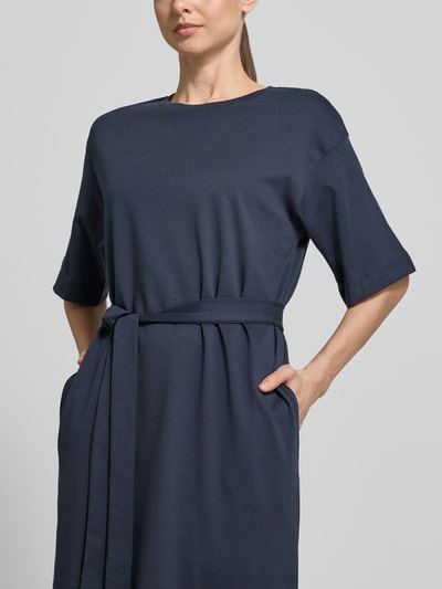 Vrouwenmodel draagt Loose Fit Maxikleid uit zuivere katoen model 'ESSENTIAL' van Selected Femme, effen, maxi, ronde hals, bindriem, korte mouw, rechte zoom, split opzij, steekzakken. Close-up bovenlichaam.