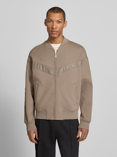 Männermodel trägt Oversized Sweatjacke aus Baumwoll-Mix Modell 'DROMZIP' von HUGO in Beige mit Reißverschluss und Logo-Patch, Ganzkörperansicht von vorne.