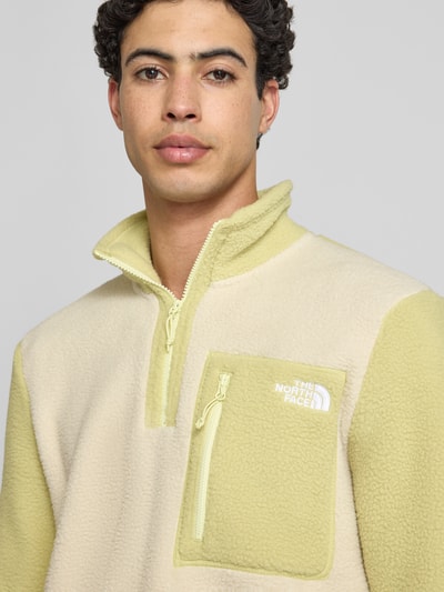 Männermodel trägt Fleecepullover mit Brusttasche Modell 'YUMIORI' von The North Face in Beige und Hellgelb, Nahaufnahme Oberkörper. Regular-Fit mit Stehkragen, Reißverschluss, Label-Stitching, Rückenlänge bei Größe M 70 cm, Ärmellänge bei Größe M 67 cm. Textur weich und flauschig.