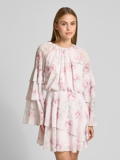 Modelka nosi Minikleid mit Volantärmeln Modell 'MAHLIIA' od Ted Baker, szyfon, krój taliowany, okrągły dekolt, rękawy z falbanami, falbana na dole, zapięcie na guzik i zamek z tyłu, długość pleców w rozmiarze 36: 39 cm, szerokość w rozmiarze 36: 44 cm, długość rękawa w rozmiarze 36: 46 cm, różowo-biały wzór z kwiatami, widok całej sylwetki z przodu.