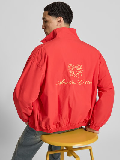 Męski model nosi Segeljacke mit Stehkragen und Logo-Stitching von ANOTHER COTTON LAB, kolor czerwony, wyhaftowane logo, bawełna, prosty krój, stójka, zamek błyskawiczny dwustronny, elastyczne wykończenia, długość tyłu w rozmiarze M: 63 cm, szerokość ramion w rozmiarze M: 60 cm, szerokość klatki piersiowej w rozmiarze M: 63 cm, długość rękawów w rozmiarze M: 55 cm, widok z tyłu na całą sylwetkę.