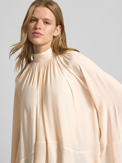 Modelka prezentuje Blusenshirt mit Stehkragen od Gina Tricot, prosty krój, marszczenia, szerokie rękawy, kremowy kolor, zbliżenie na górę.