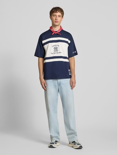 Männermodel trägt Relaxed Fit T-Shirt aus reiner Baumwolle von Champion, blau-weiß mit Logo-Print, Rundhalsausschnitt, Ganzkörperansicht von vorne.
