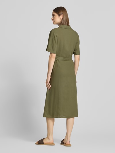Modelka nosi oliwkowe, jednokolorowe, midi, luźno dopasowane Freizeitkleid aus Viskose-Leinen-Mix Modell 'PIA' od Pieces, krótki rękaw, kieszeń na piersi, guziki, widok całej sylwetki z tyłu.
