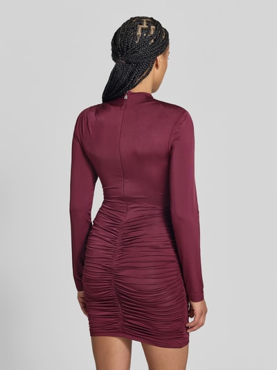 Frauenmodel trägt Slim Fit Minikleid aus Viskose-Mix von ROTATE in Bordeaux mit Raffungen, Stehkragen, langärmelig, Ganzkörperansicht Rückansicht.