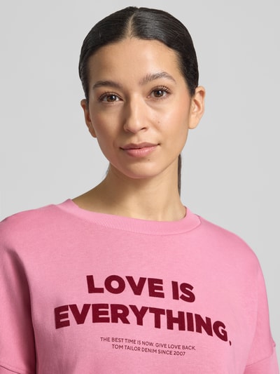 Frauenmodel trägt Regular Fit Sweatshirt aus reiner Baumwolle von Tom Tailor Denim in Rosa mit Label-Schriftzug, Nahaufnahme Oberkörper.