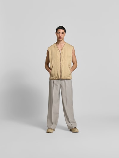 Männermodel trägt Relaxed Fit Weste in Stepp-Optik von MM6 Maison Margiela, beige, V-Ausschnitt, Eingrifftaschen, Reißverschluss, Ganzkörperansicht von vorne. Rückenlänge bei Größe 50: 70 cm, Taillenweite: 61 cm.