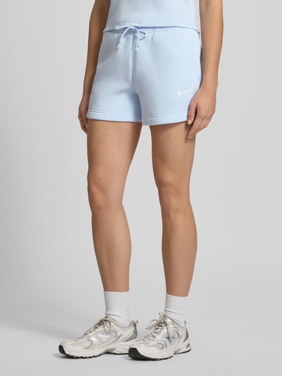 Frauenmodel trägt Sweatshorts mit Logo Modell 'Phoenix' von Nike aus Baumwoll-Mix in Hellblau, Regular-Fit, sichtbarer Tunnelzug am elastischen Bund, glatte Textur, Ganzkörperansicht von vorne. Bundweite bei Größe S: 38 cm, Innenbeinlänge: 10 cm.