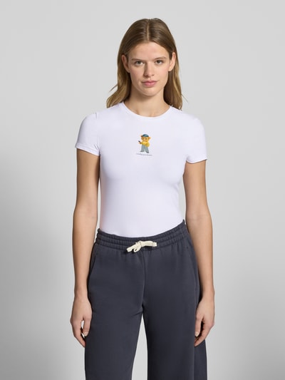 Kobiece model prezentuje Damski t-shirt Slim Fit T-Shirt mit Logo-Print Model 'Sweet' od REVIEW, elastyczna mieszanka bawełny, krój slim fit, nadruk z logo, okrągły dekolt, długość tyłu w rozmiarze S: 52 cm, jednolity biały, kolorowy nadruk, gładka tekstura, widok całej sylwetki z przodu.