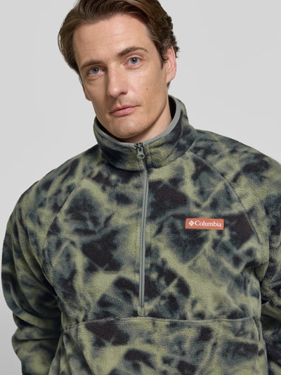 Männermodel trägt Fleecepullover mit Label-Details Modell 'Timber Crest™' von Columbia, grün-schwarzes Muster, Nahaufnahme Oberkörper. Gerader Schnitt, Stehkragen, Reißverschluss, Rückenlänge 70 cm, Ärmellänge 73 cm.