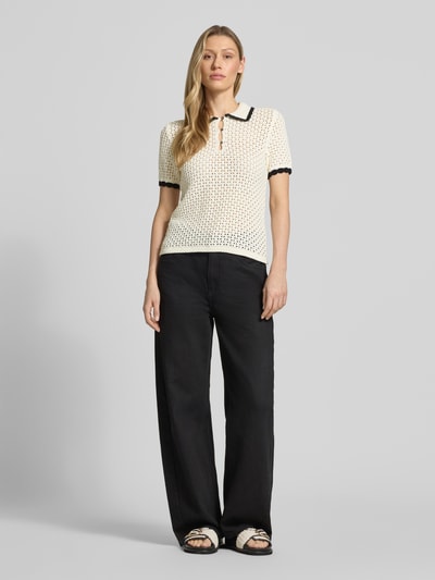 Vrouwenmodel draagt Slim Fit Poloshirt in Strick-Optik van Jake*s Casual, katoen, polokraag, korte mouwen, gebreide look, opengewerkt patroon, elastische boorden, lengte achteraan 53 cm, mouwlengte 24 cm, kleuren crème en zwart, helemaal zwart broek, sandalen, Ganzkörperansicht van voren.