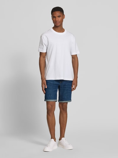 Männermodel trägt blaue Slim Fit Jeansshorts aus Baumwoll-Mix Modell 'NAAILO' von Armedangels, Denim-Optik, 5-Pocket-Design, Label-Patch, Ganzkörperansicht von vorne.