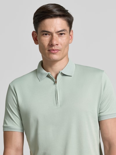 Męski model nosi Regular Fit Poloshirt aus Bio-Baumwoll-Mix Modell 'FAVE' von SELECTED HOMME, jednokolorowy, aplikacja: naszywka z logo, kołnierzyk polo, zamek błyskawiczny, krótki rękaw, wykończenie: dżersej interlock, materiał: mieszanka bawełny ekologicznej, Nahaufnahme górnej części ciała.