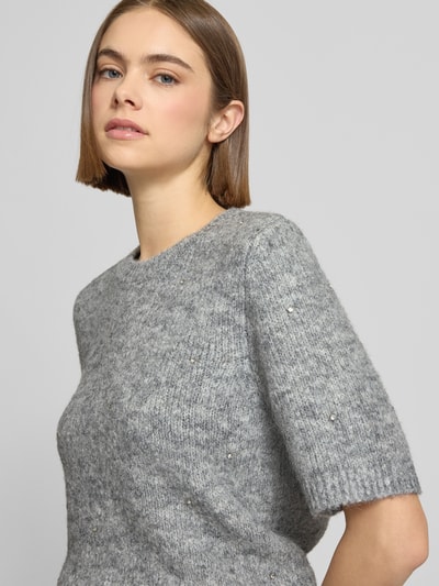 Frauenmodel trägt Strickpullover mit 1/2-Arm und Rundhalsausschnitt von Gina Tricot, grau meliert, Material-Mix mit Lanawoll-Anteil, Ziersteinbesatz, Regular-Fit, Nahaufnahme Oberkörper.