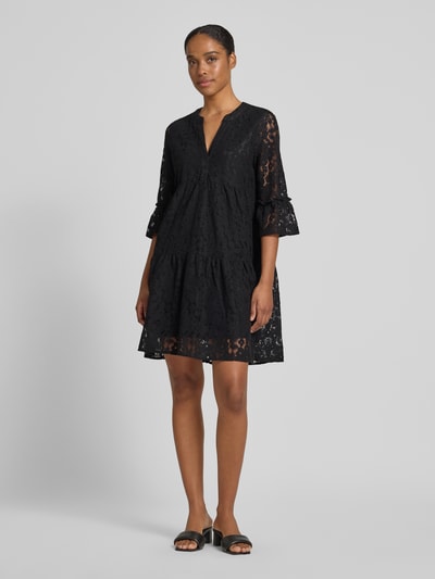 Frauenmodel trägt Loose Fit Spitzenkleid aus Baumwoll-Mix Modell 'HONEY' von Vero Moda, Optik: Unifarben, Spitzen-Muster, V-Ausschnitt, 3/4-Arm, Glockenärmel, knielang, Materialverarbeitung: Spitze, Farbe Schwarz, Ganzkörperansicht von vorne.