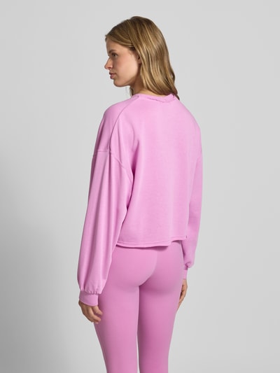 Frauenmodel trägt Cropped Sweatshirt mit Logo-Stitching von Nike in Rosa mit Relaxed-Fit, Rundhalsausschnitt, elastische Ärmelabschlüsse, Ganzkörperansicht Rückansicht.