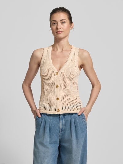 Kobiece model prezentuje kamizelkę dzianinową z dekoltem w serek model 'LASTICE' od Marella, czysta bawełna, krój slim fit, listwa guzikowa, długość tyłu w rozmiarze S: 56 cm, jasny beż, faktura ażurowa, przód, ujęcie całopostaciowe z przodu.